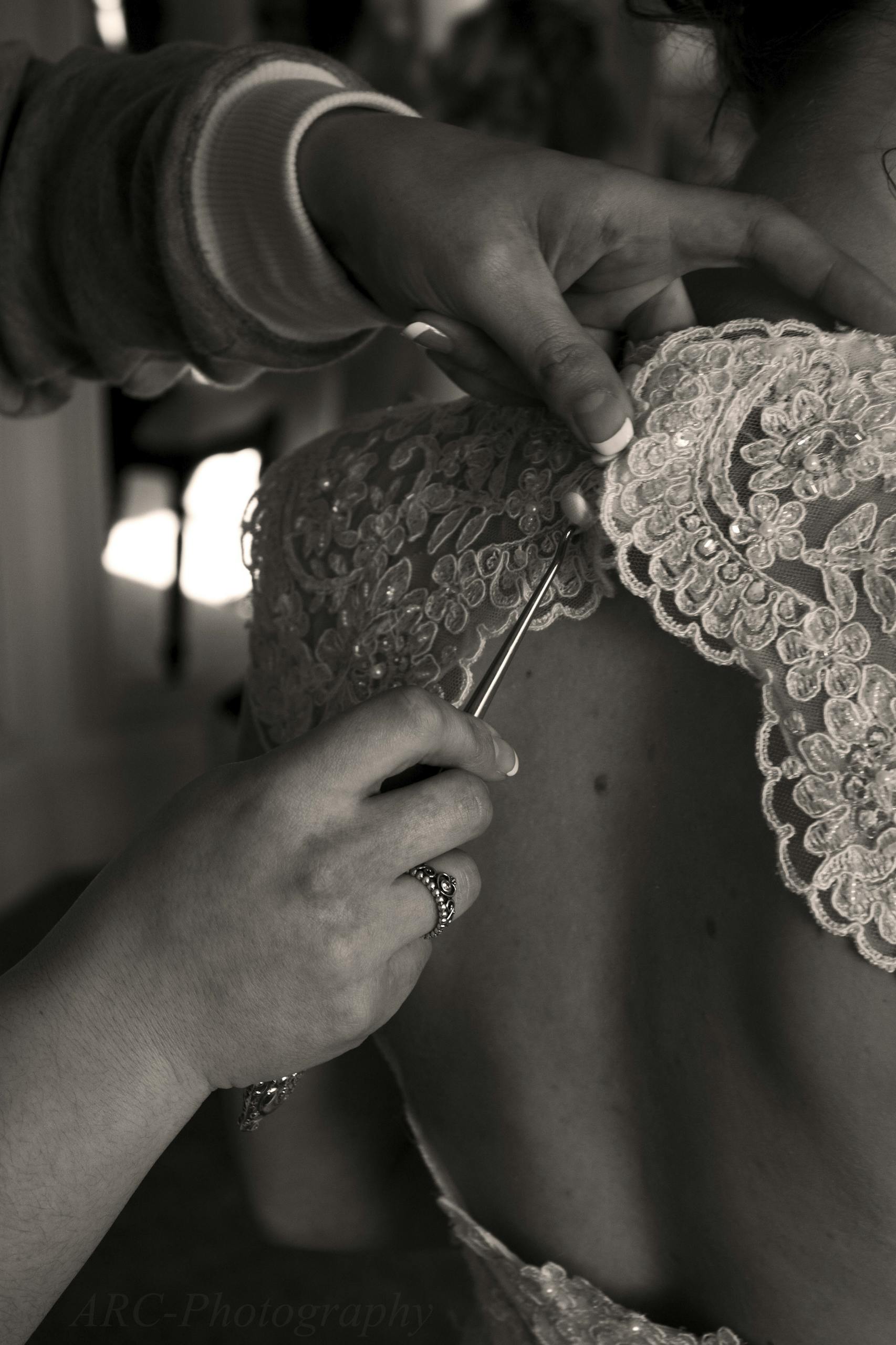 A detailed view of hands sewing intricate lace designs on a bridal dress.