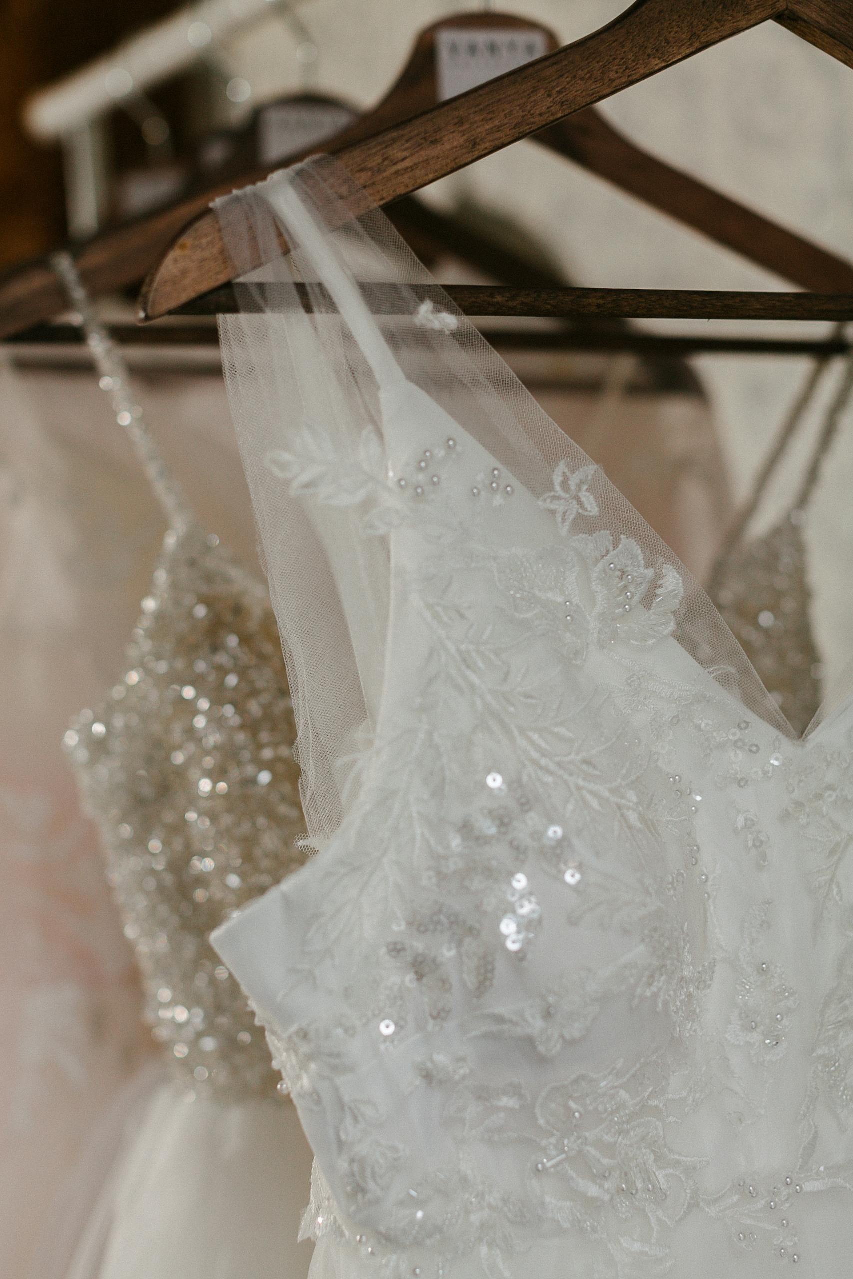 Close-up of elegant wedding dresses featuring sequins and lace details on hangers.